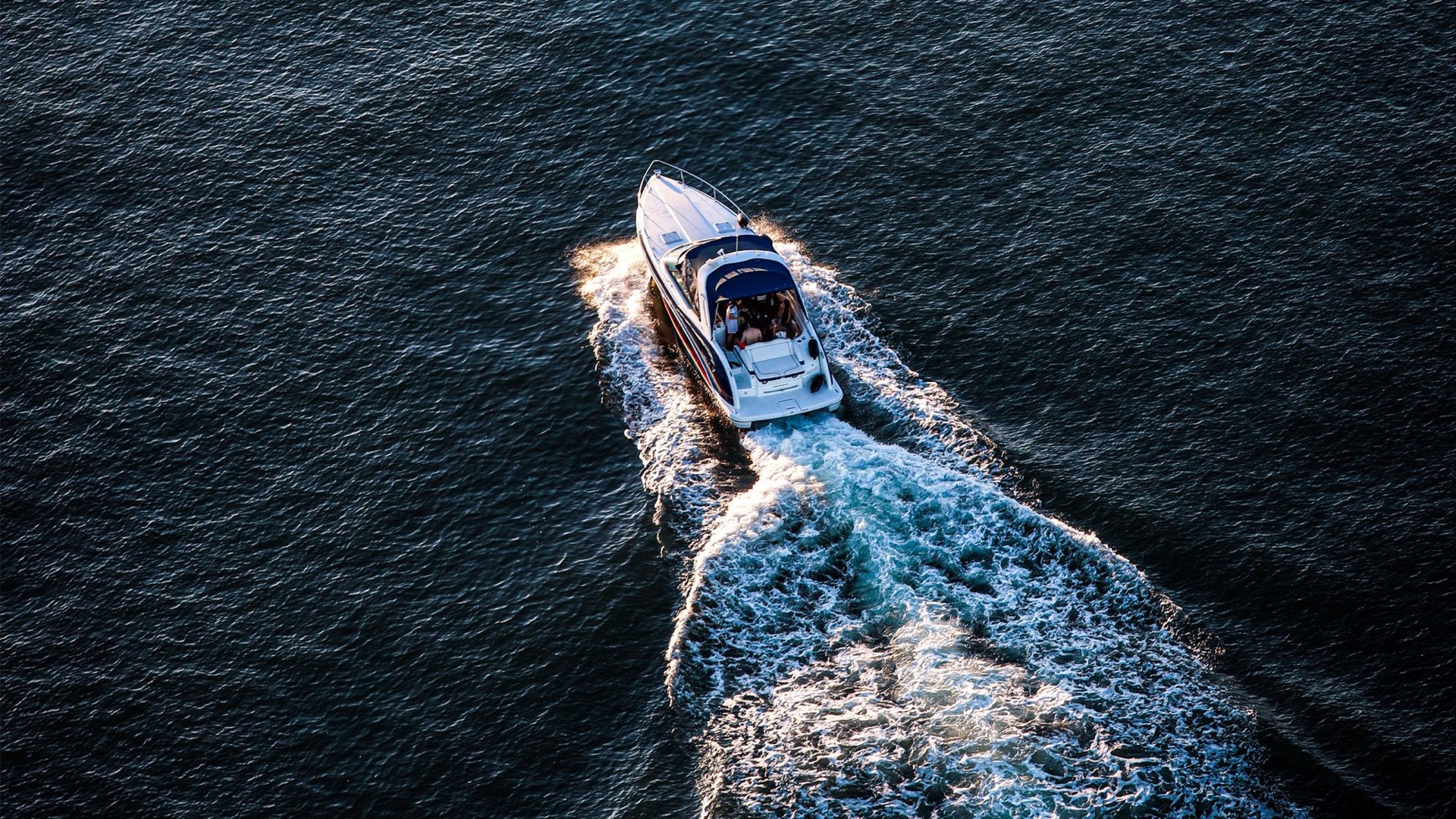 A motor cruiser at speed, trailing white wake across dark water