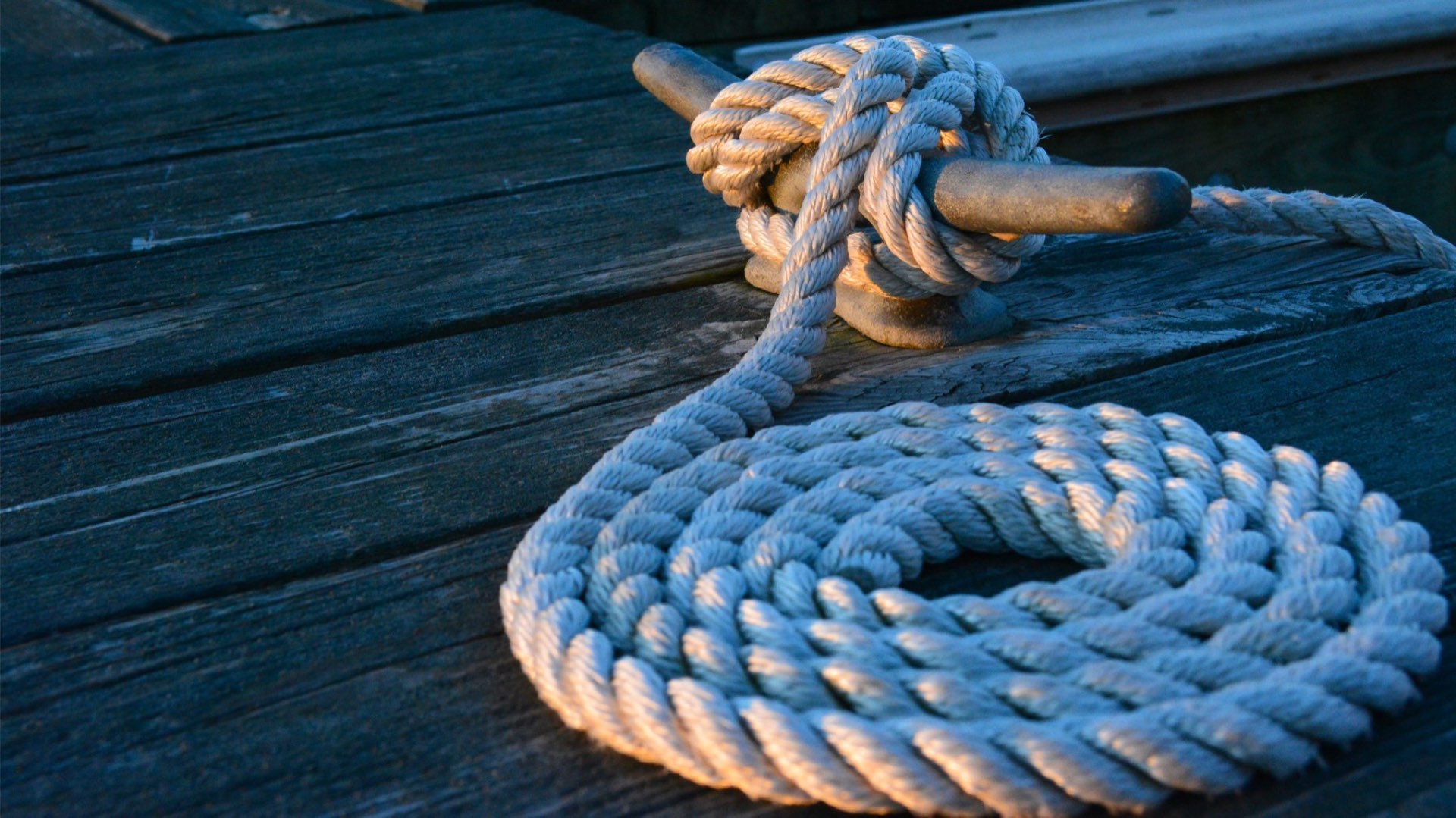 A mooring line made fast to a cleat and coiled on a weathered wooden pontoon in evening light