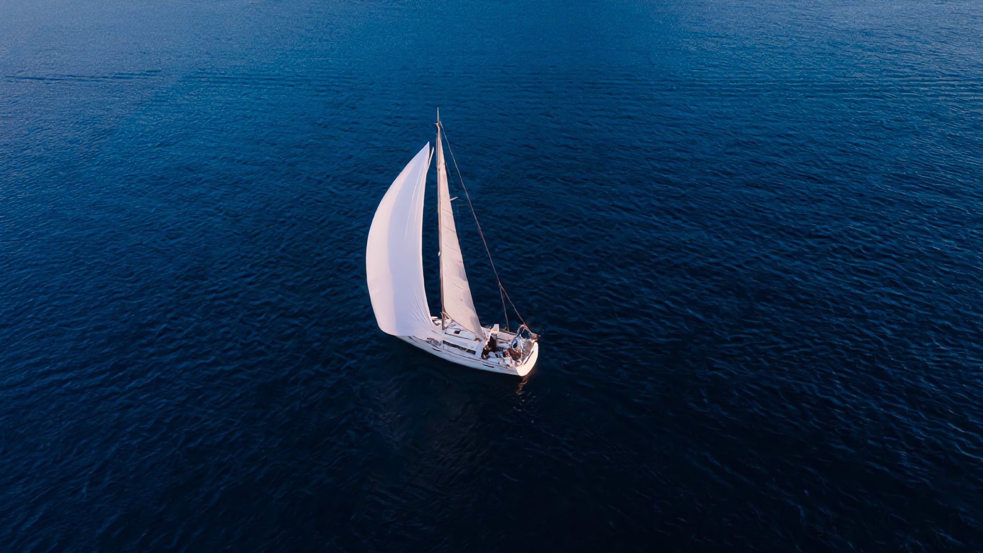 A yacht under full sail seen from above on deep blue water