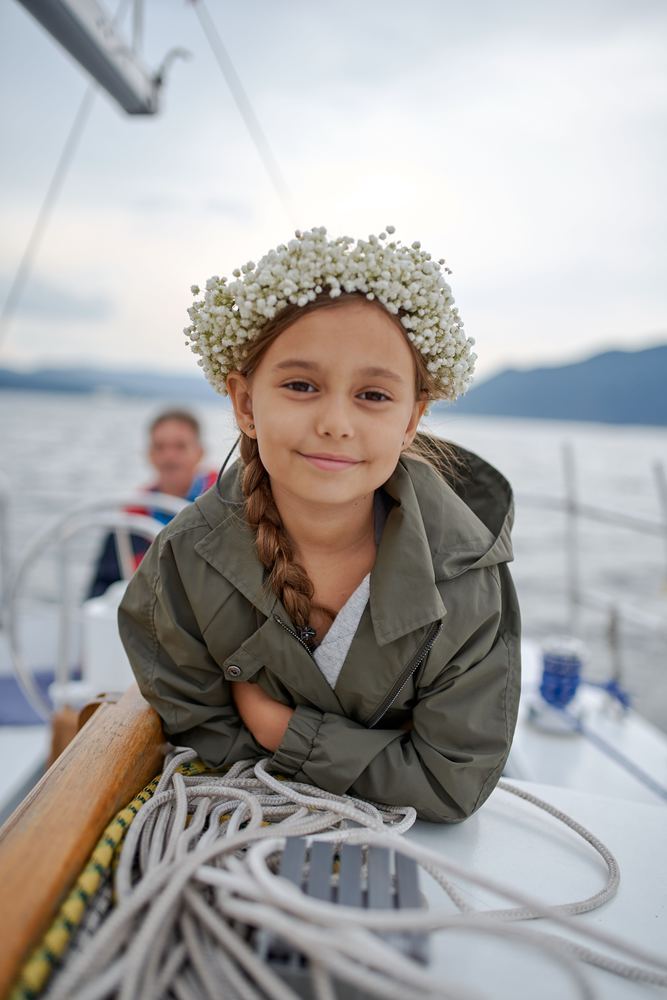 A child in a flower crown sitting on the foredeck of a yacht