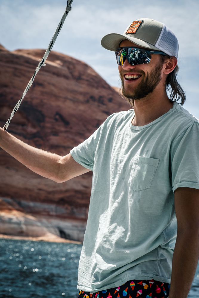 A sailor holding the rigging, cliffs rising behind the boat