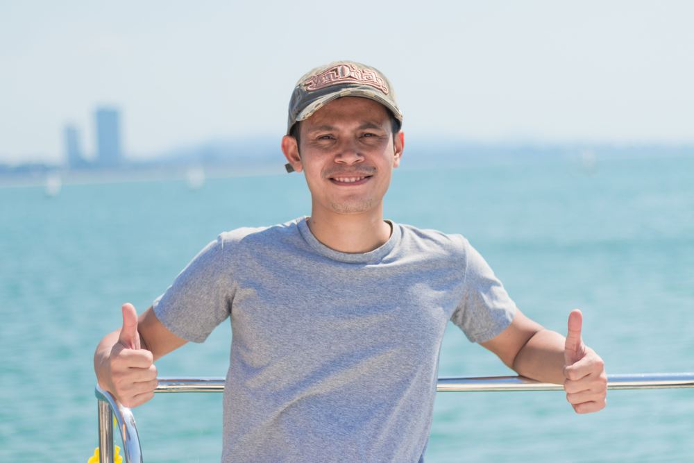 A man on deck giving a thumbs up in front of turquoise water